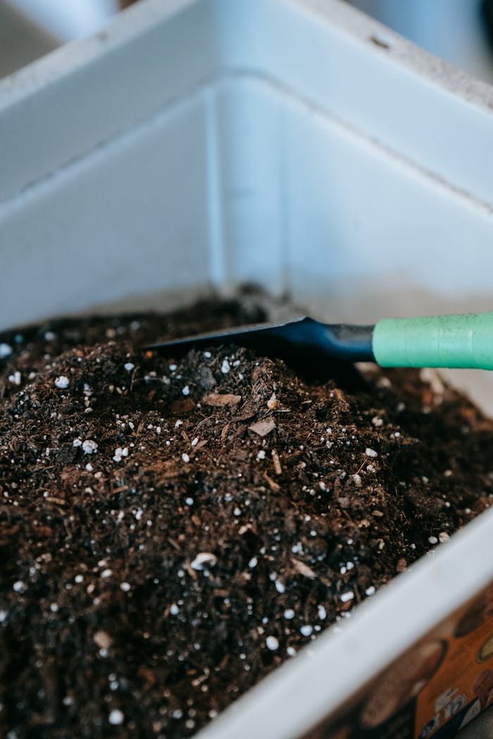 Gardening soil with a green-handled trowel in a white container, perfect for planting.